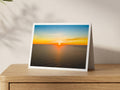 Premium A5 greeting card showing an orange sunset over the Atlantic off Porthcothan Bay, with The Quies on the horizon