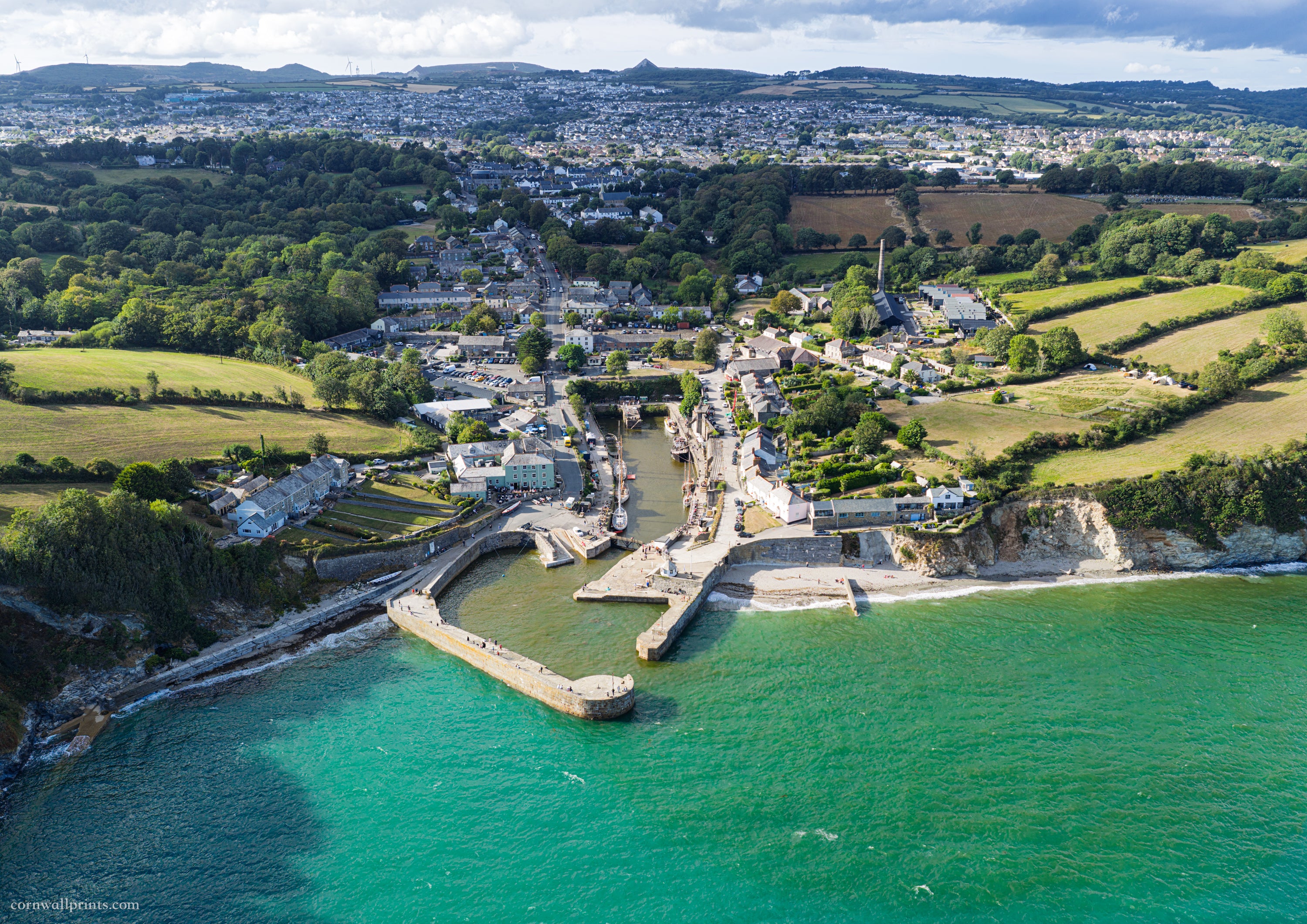 Aerial view over Charlestown Harbour looking inland to St Austell and the Sky Tip, with turquoise sea contrasting with rain run-off water inside the harbour