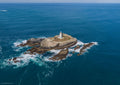 Close aerial view of Godrevy Lighthouse, enclosing stone walls and rugged island rocks surrounded by blue sea and white surf