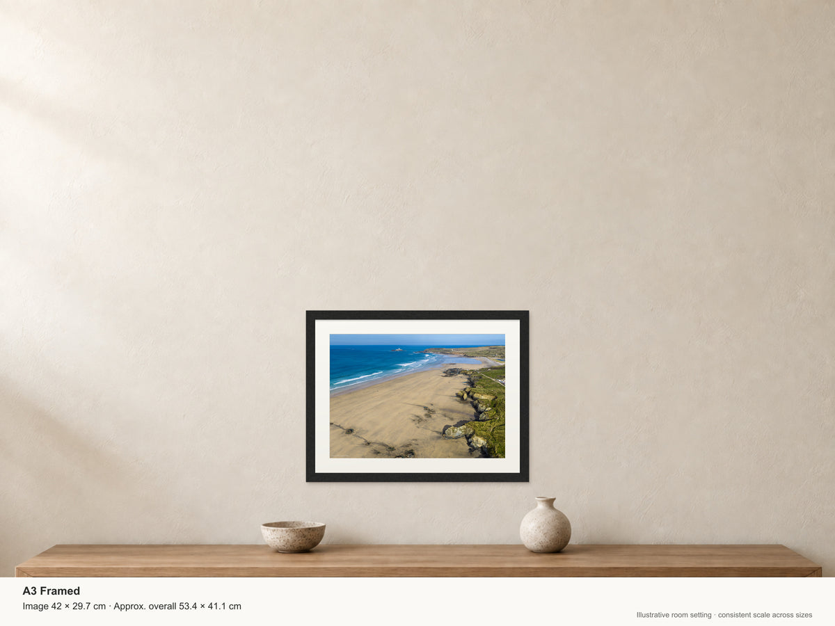 Expansive Gwithian beach with golden sand, textured cliffs, clean offshore surf and surfers, looking north towards Godrevy Lighthouse — A3 22mm black stained frame and 35mm mount. Illustrative room view with dimensions.