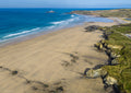 Expansive Gwithian beach with golden sand, textured cliffs, clean offshore surf and surfers, looking north towards Godrevy Lighthouse