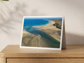 Hayle Estuary sandbanks and clean autumn surf towards Gwithian and Godrevy Lighthouse, shown on an A5 greeting card with a white border on an oak sideboard