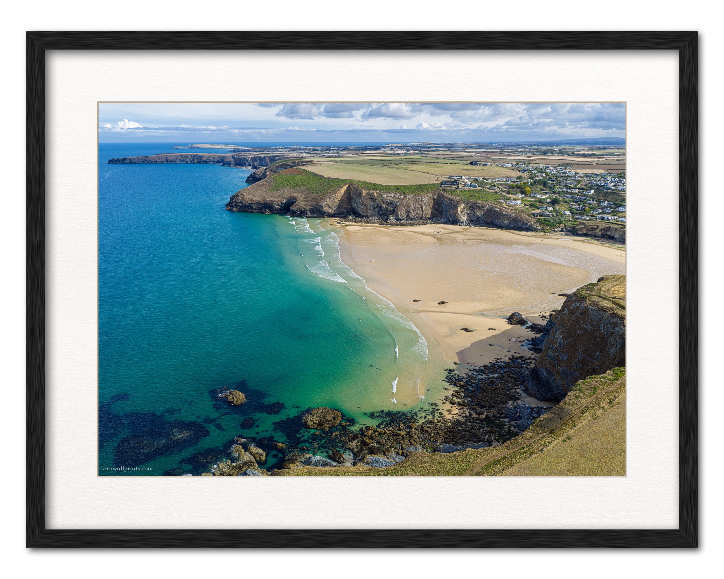 Mawgan Porth aerial photograph looking north from the sea across turquoise water and low-tide sand, displayed in a black frame with white mount