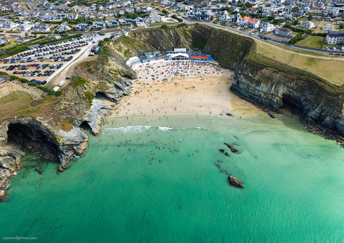 Aerial view of Lusty Glaze Beach, Newquay, with clear green-blue water, swimmers and the sheltered sandy cove at mid tide