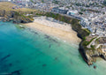 Aerial view of Tolcarne Beach, Newquay, with clear turquoise water, swimmers, pale sand and cliffside beach huts at mid tide