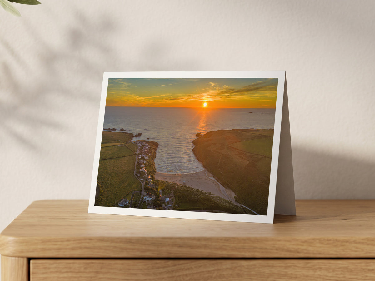 Premium A5 greeting card showing the sun setting over Porthcothan Bay between green headlands