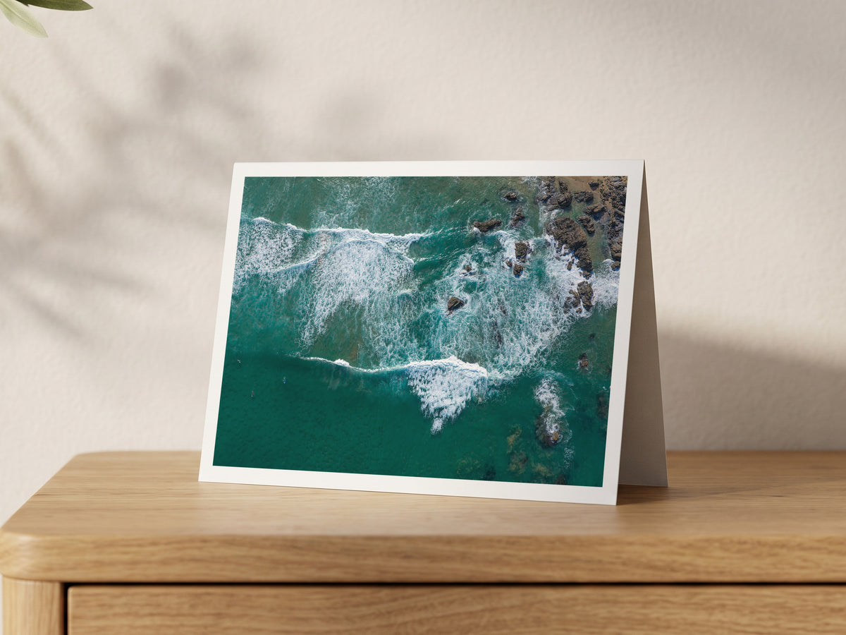 Premium A5 greeting card showing surfers beside rocks and white water at Porthcothan Bay from above