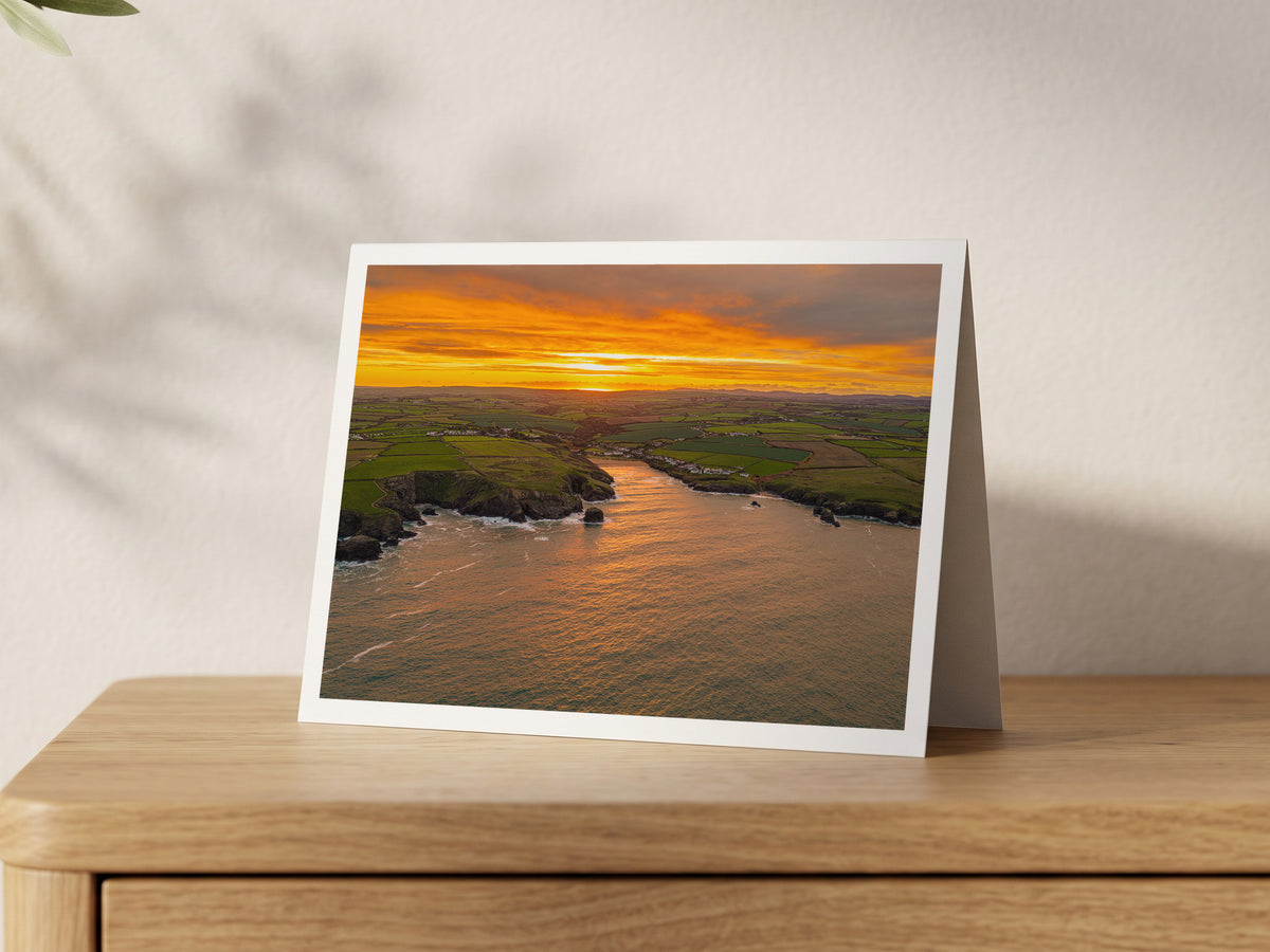 Premium A5 greeting card showing a golden sunrise over Porthcothan Bay, with the sun's path across the water into the bay