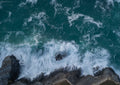 Top-down aerial view of Fox Cove at dusk, with slow-shutter white surf swirling over dark rocks and deep teal Atlantic water.