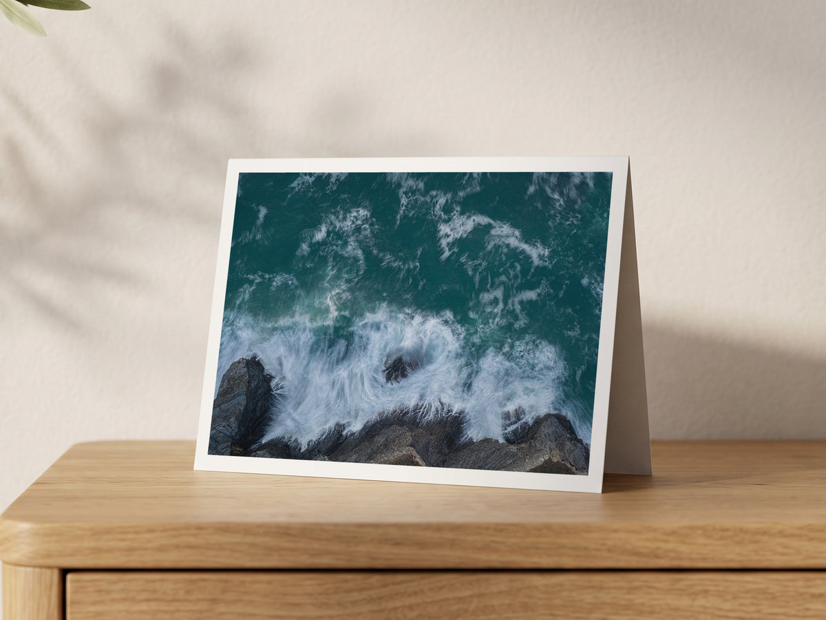Premium A5 greeting card showing slow-shutter surf swirling over dark rocks at Fox Cove from above