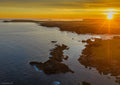 Summer solstice sunrise along Cornwall’s Seven Bays coast, with dark rocks, blue-grey sea and golden fields towards Trevose Head.
