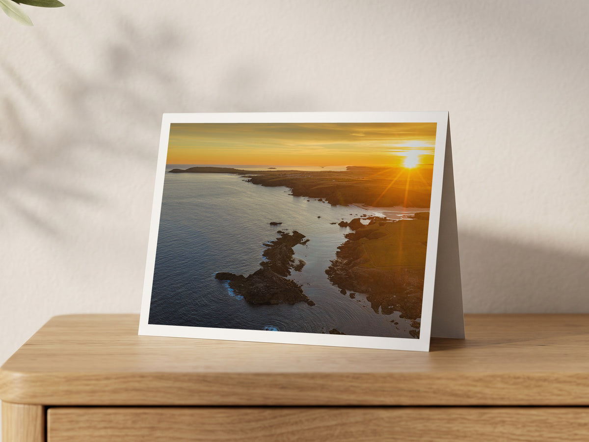 A5 greeting card with a white border around a photograph of summer solstice sunrise over Cornwall’s Seven Bays coast, displayed on an oak sideboard.