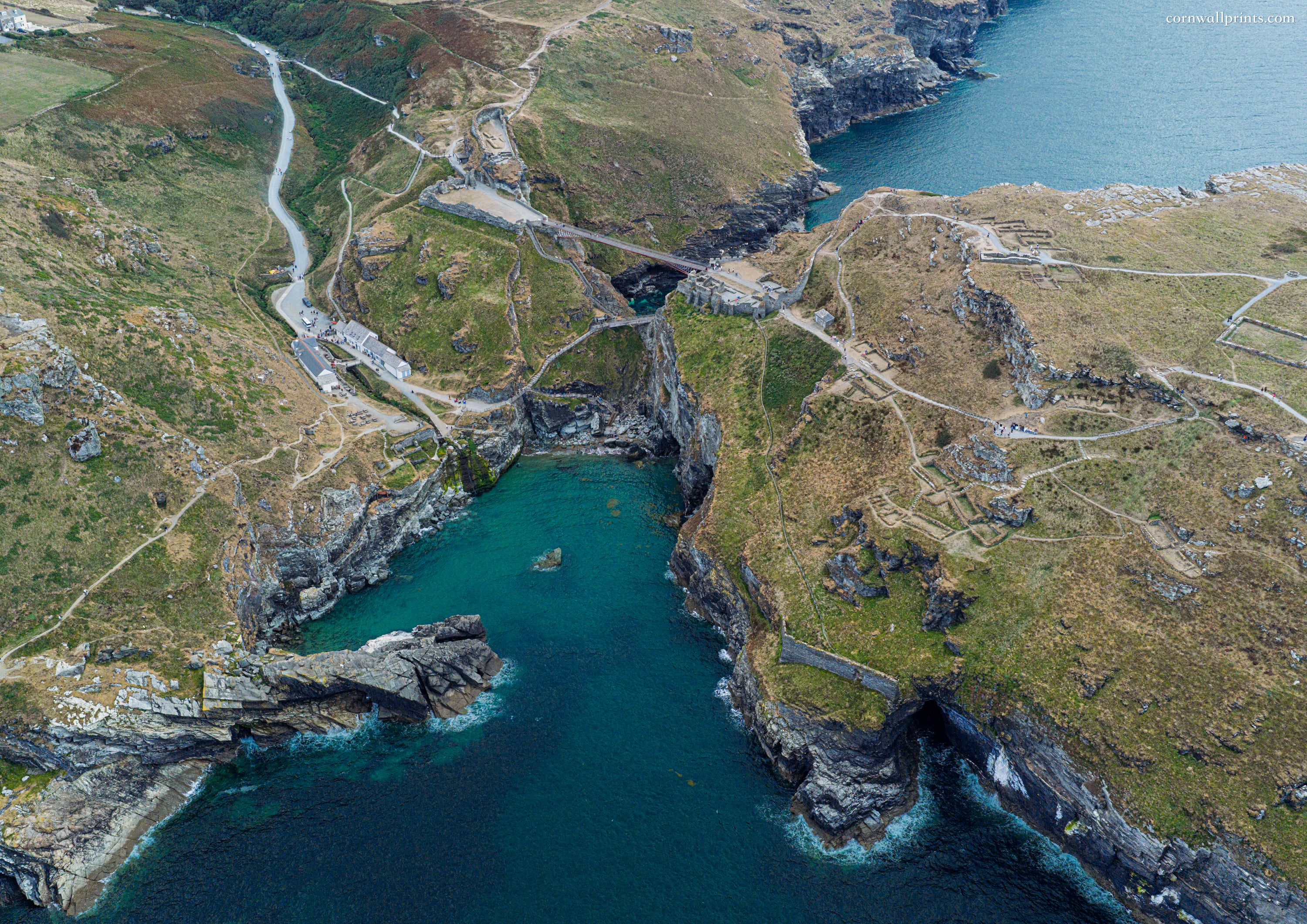 Aerial view of Tintagel Castle island ruins, footbridge and turquoise sea