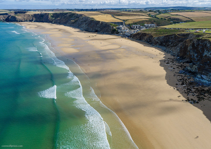 Aerial view looking north across Watergate Bay at low tide with turquoise water, golden sand and dark cliffs