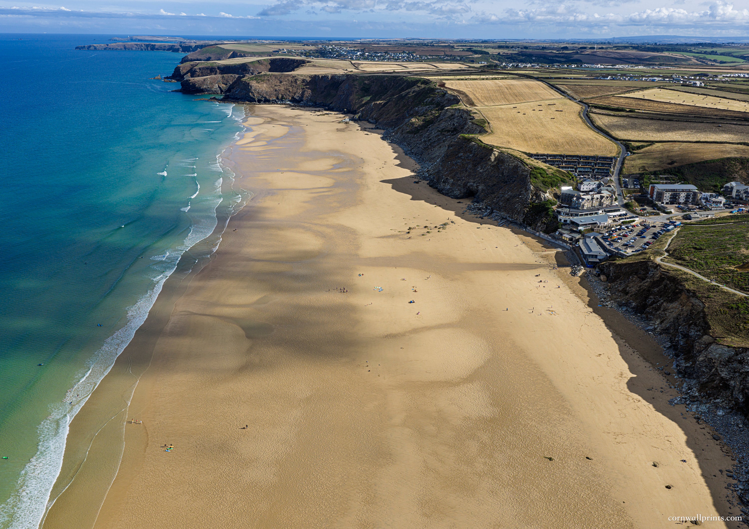 Aerial view looking north along Watergate Bay with expansive low-tide sand, turquoise water and rugged cliffs