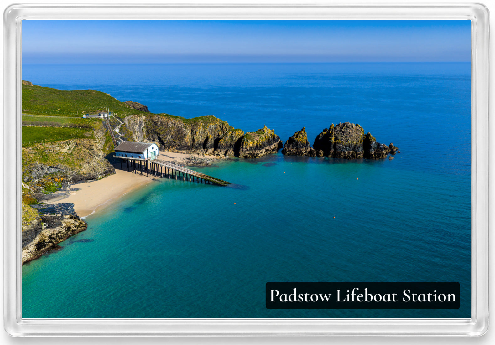 Padstow Lifeboat Station fridge magnet showing the station and slipway at Mother Ivey’s Bay beside turquoise water and rocky islets